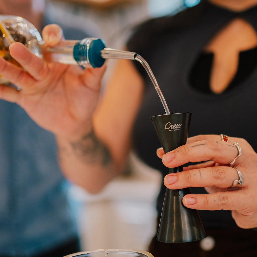 A person pouring alcohol into a good measure jigger, which is part of our bar tool set.